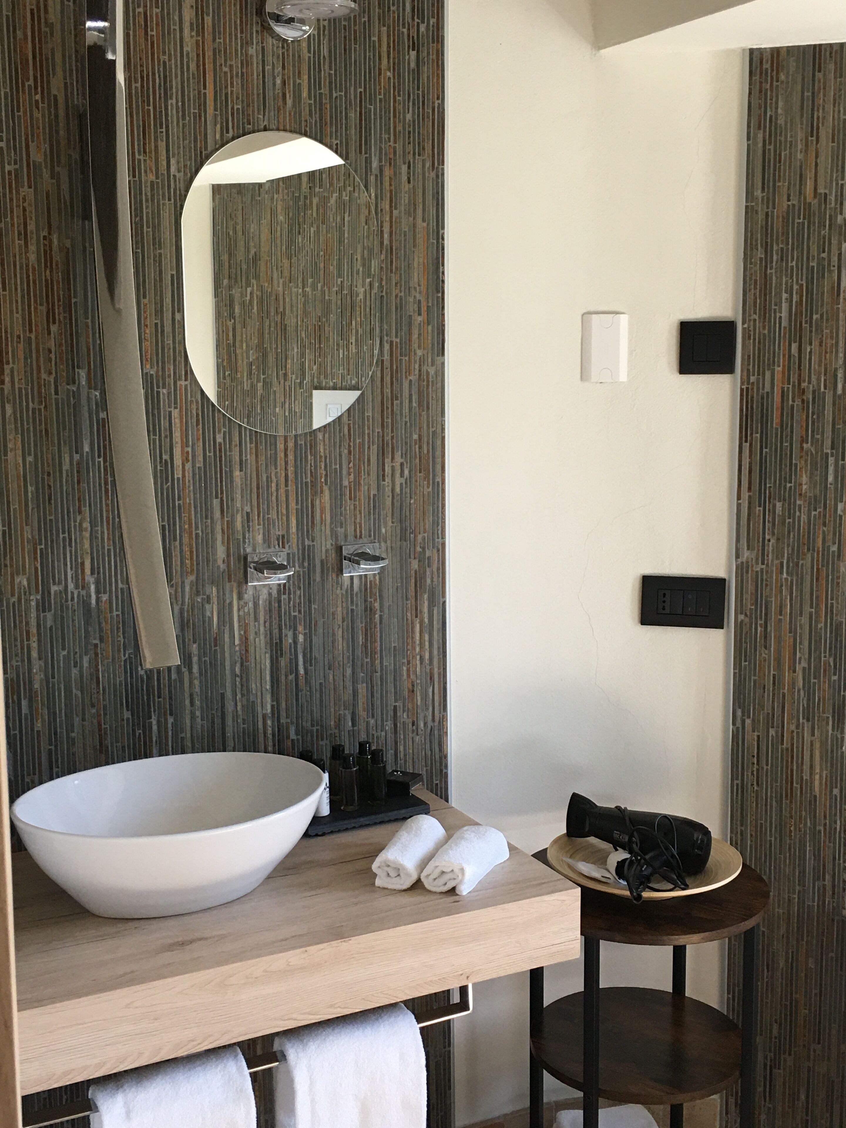 A modern bathroom with a large vessel sink, a round mirror, and a small round table with towels.