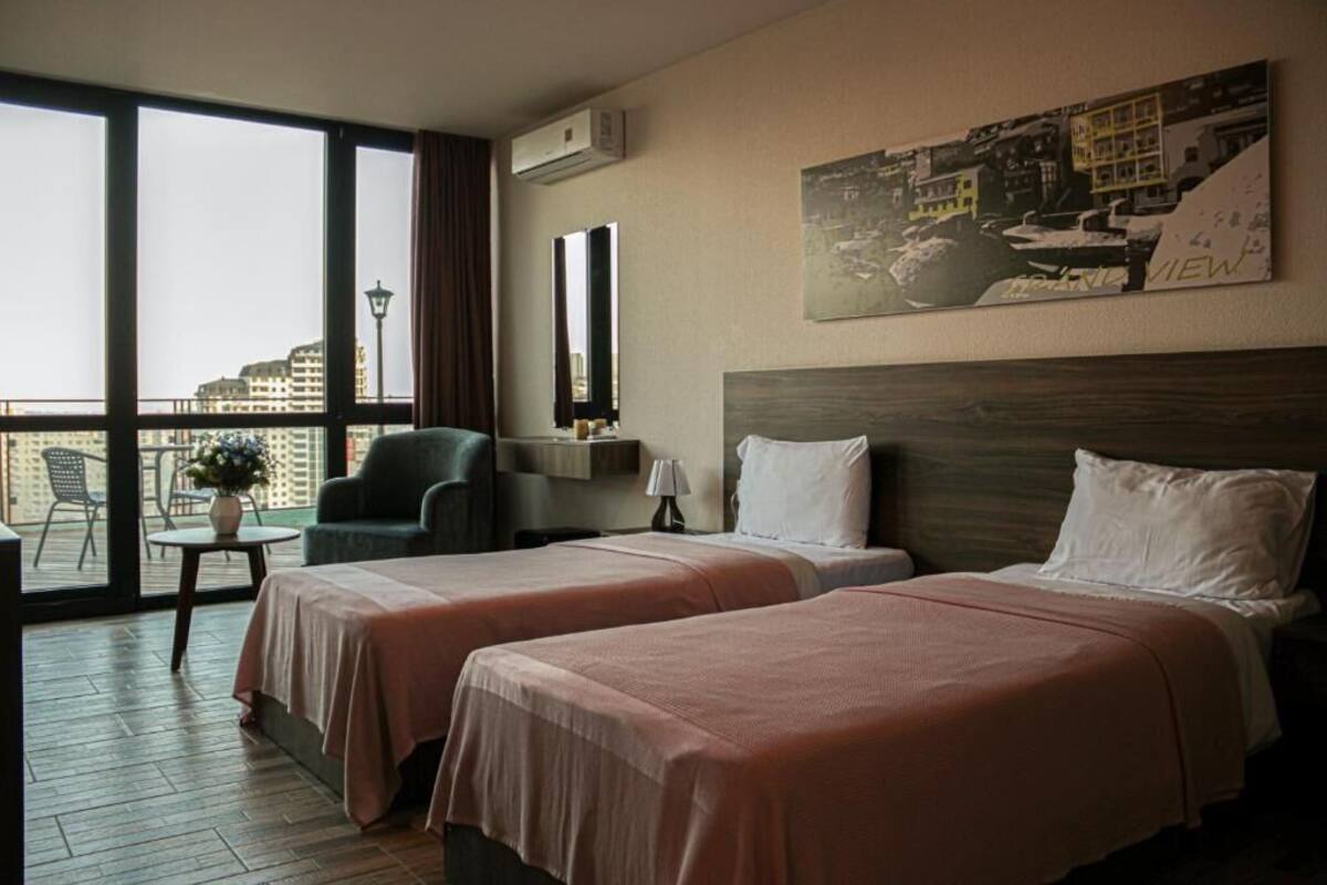 A hotel room with two beds, a balcony, a cityscape view, and a painting on the wall.