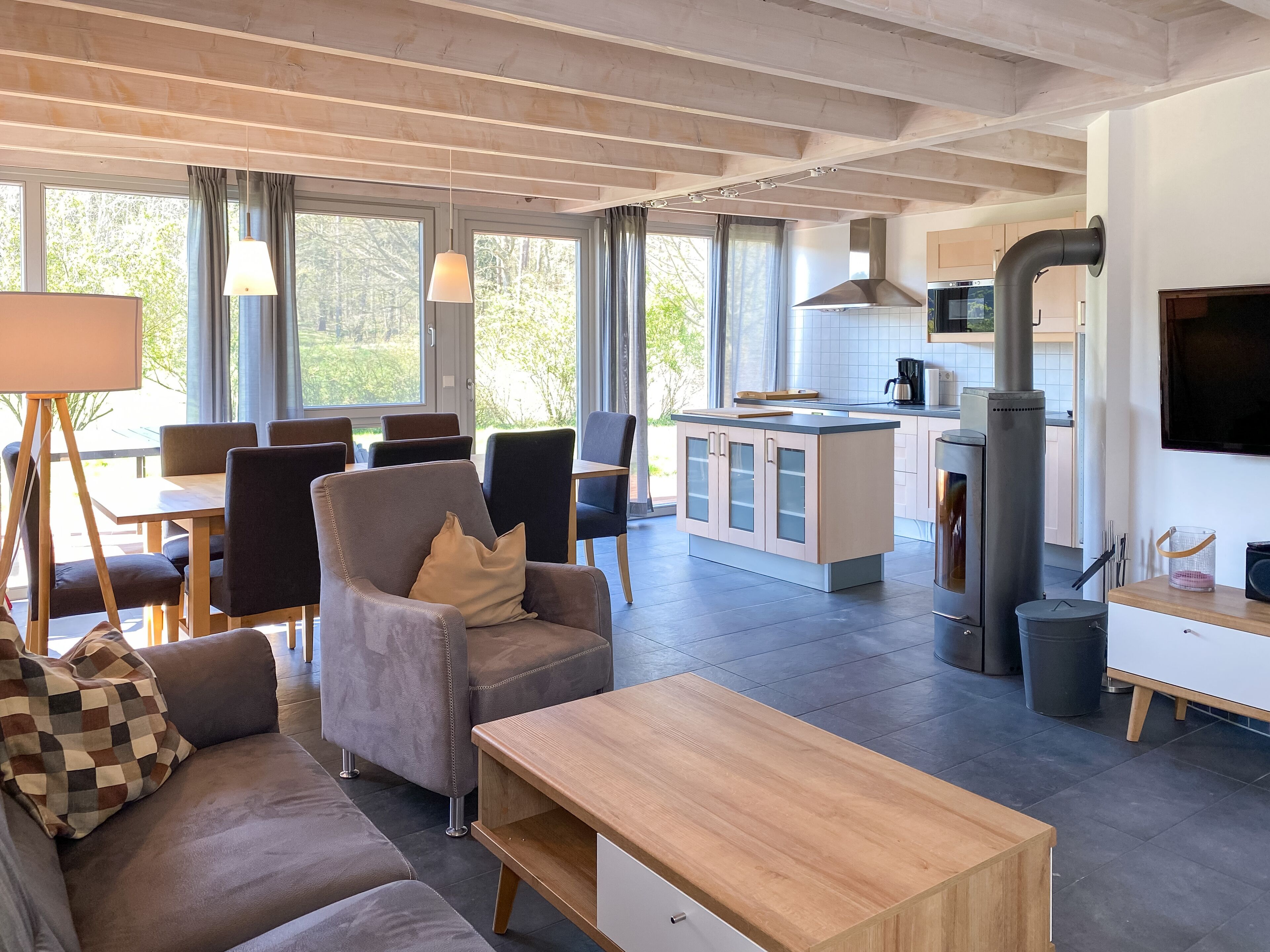 Un salon moderne avec un canapé, une table basse et un coin repas avec des chaises. On aperçoit une cuisine équipée d’une cuisinière et de placards au fond.