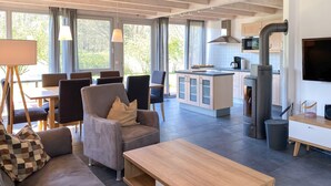 Un salon moderne avec un canapé, une table basse et un coin repas avec des chaises. On aperçoit une cuisine équipée d’une cuisinière et de placards au fond.