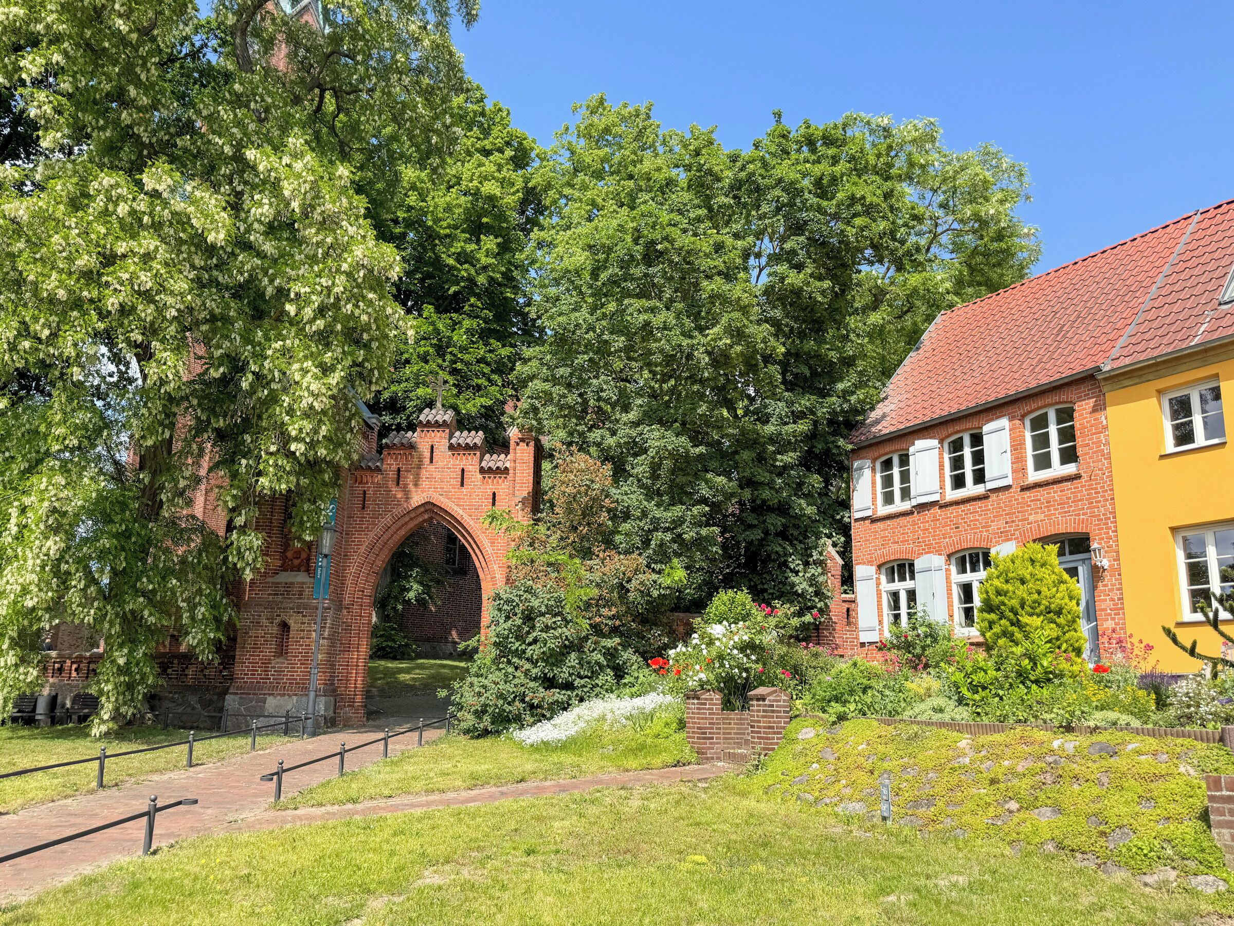Ein Backsteinbogen, ein gelbes Gebäude und üppiges Grün.