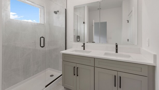 Un baño moderno con ducha de vidrio, dos lavamanos, un espejo grande y muebles de color claro.