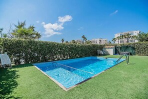 Une piscine rectangulaire avec un escalier en métal sur un de ses côtés, entourée de gazon synthétique vert.