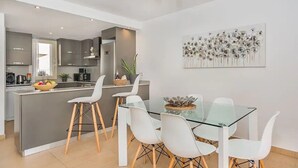 Une cuisine moderne avec des meubles gris, un îlot central et un coin repas comprenant une table en verre et des chaises blanches.