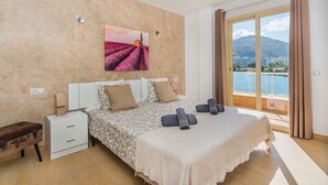 Une chambre à coucher avec un lit, une table de chevet, une valise, un tableau et un balcon avec vue.