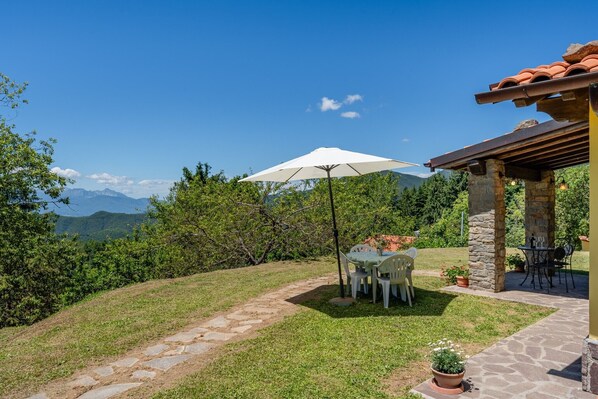 A patio with a table and chairs, a white umbrella, stone pillars, and a view of mountains.