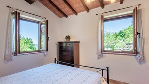 Ein Schlafzimmer mit einem Bett, zwei mit Vorhängen versehenen Fenstern, einem Schminktisch und einer Deckenleuchte.