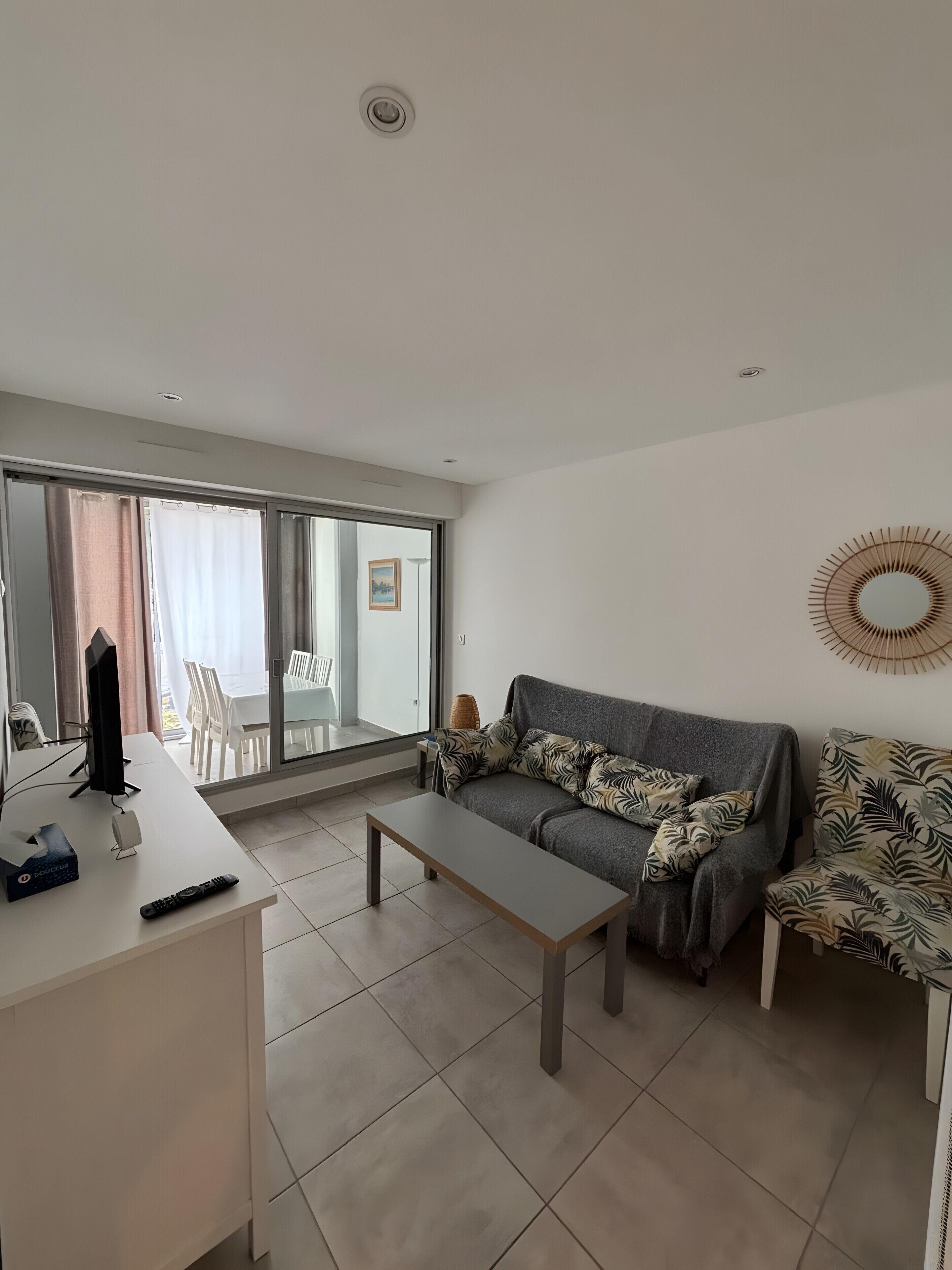 A modern living room with a sofa, a coffee table, a TV, and a dining area with chairs and a table.