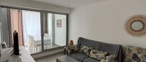A modern living room with a sofa, a coffee table, a TV, and a dining area with chairs and a table.