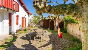 A courtyard with a table and chairs, a tree, and a building with red shutters. - Fully Renovated and Air-Conditioned T3 Apartment in Southern Basque Country and Landes (Tarnos)