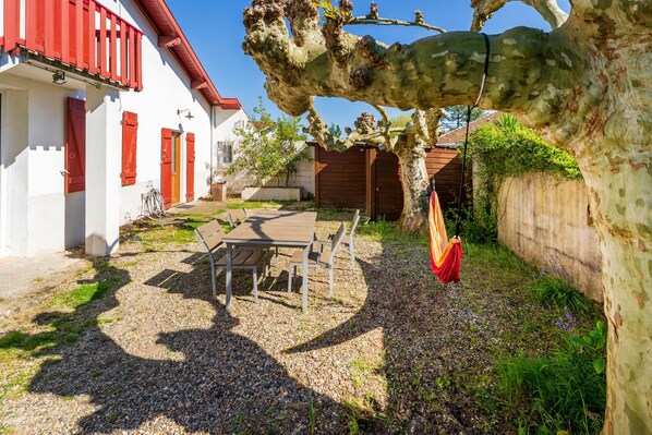 A courtyard with a table and chairs, a tree, and a building with red shutters.