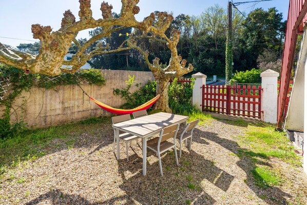 Une terrasse avec une table et des chaises, un hamac et un portail rouge.