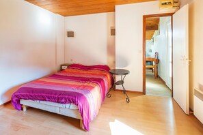 Une chambre à coucher avec un lit, une petite table et une porte donnant sur une autre pièce.