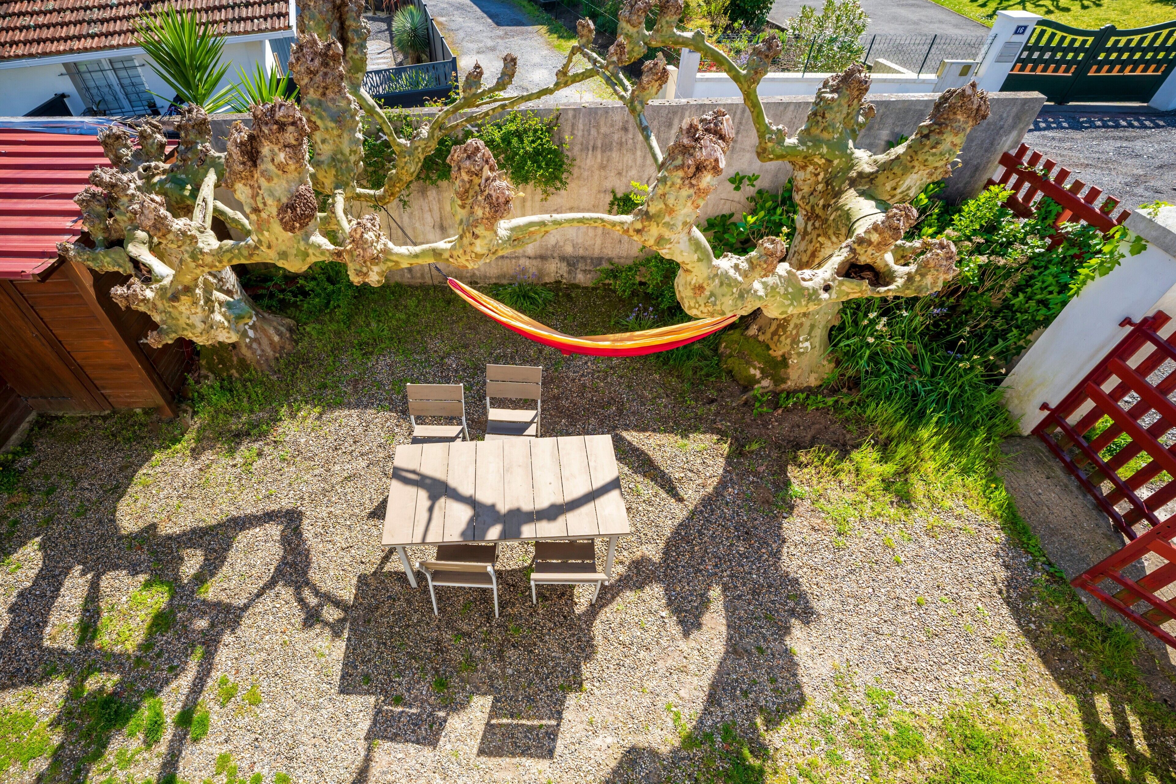 A hammock between two trees, a wooden table with chairs, and a gravel patio.