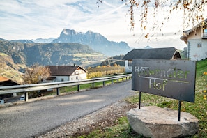 Uma estrada rural com uma placa indicando 'Rottwandler Hof' e montanhas ao fundo.