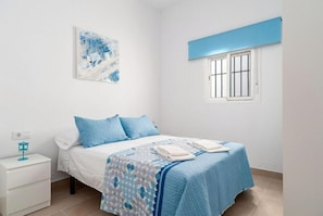 Een slaapkamer met een bed, nachtkastje, raam en een aan de muur hangend kunstwerk.
