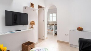 A modern living room with a flat-screen TV, a small table with a lamp, and a basket of fruit on a counter. - Casa Carmen (Vejer de la Frontera)