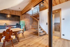 A modern kitchen with wooden accents, a dining area with a wooden table and chairs, and a staircase leading to an upper level.