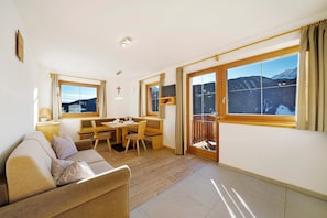 Una habitación con sofá, mesa de comedor, sillas, televisor y un amplio ventanal con vista a la montaña.