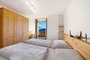 Un dormitorio con un armario de madera, una cama con ropa de cama blanca, cabecero de madera y vistas por una ventana.