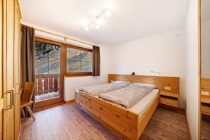 Un dormitorio con cama de madera, un escritorio y una ventana con vista a una terraza de madera.