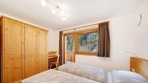 Un dormitorio con dos camas, un armario de madera, un escritorio y una ventana con cortinas.