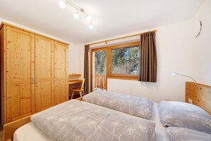 A bedroom with two beds, a wooden wardrobe, a desk, and a window with curtains.