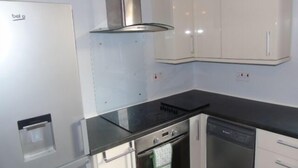 A kitchen with a stove, oven, and dishwasher, white cabinets, and a stainless steel range hood. - Snug - Abhainn Apartment (Helensburgh)