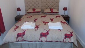 A bed with a patterned bedspread, two matching pillows, and two bedside tables with lamps. - Snug - Abhainn Apartment (Helensburgh)