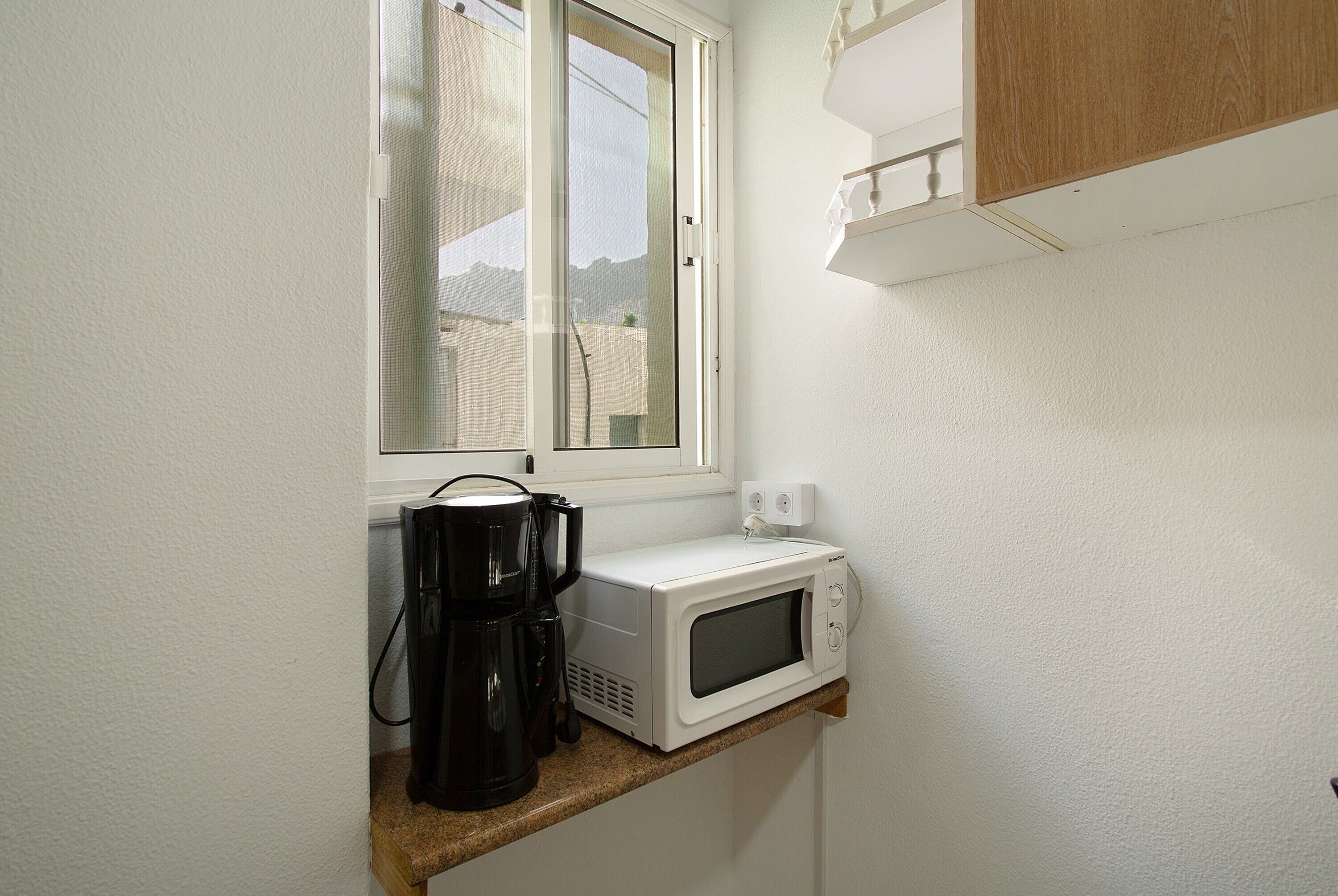 Una cocina con ventana, cafetera y microondas en la encimera.