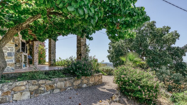 Un bâtiment en pierre doté d’un espace extérieur abrité, entouré de gravier et de différentes plantes.
