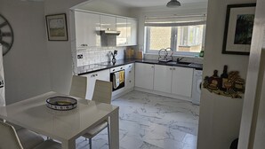 A compact kitchen with white cabinets, a marble countertop, and a dining table with chairs. - Snug - Colquhoun Square Apartment (Helensburgh)