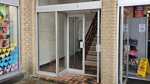 A building with a brick facade, a glass entrance, and a tiled ground. - Snug - Colquhoun Square Apartment (Helensburgh)