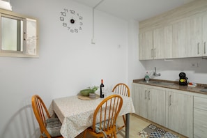 Un comedor con una mesa dispuesta para dos personas, un reloj en la pared y armarios al fondo.