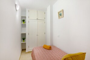 Une chambre à coucher avec un lit, une armoire et deux plantes en pot disposées sur des étagères.