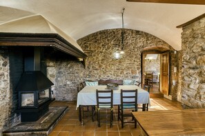 A stone-walled room with a fireplace, a dining table with chairs, and a wooden ceiling. - Country House 'Mas Cases' with Mountain View, Private Pool and Wi-Fi (Regencós)