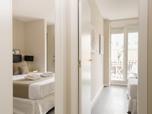 Una habitación de hotel con una cama, una mesita de noche con lámpara y un balcón con barandilla.