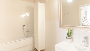 A modern bathroom with a glass-enclosed shower, a white vanity with a mirror, and a potted plant.