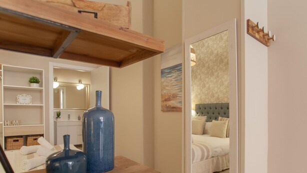 A modern bedroom with a large mirror, a bed with a tufted headboard, and a wooden shelf with decorative items.