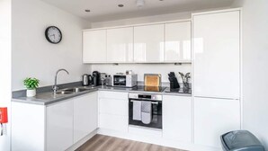 Una cocina moderna con armarios blancos, horno empotrado, cafetera y un reloj en la pared.