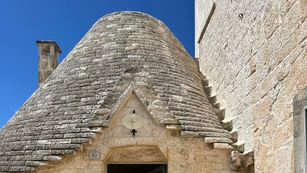 A stone building with a tiled roof, a door, and two lounge chairs outside. - iCONICO - Authentic Trulli Experience (Cisternino)