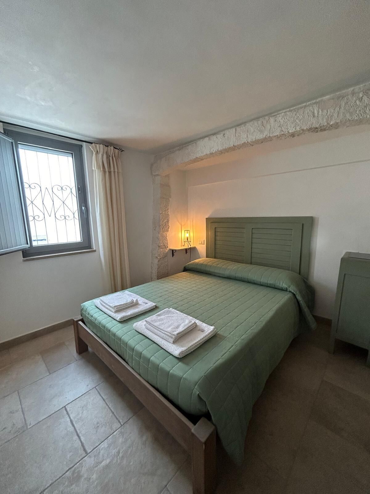 A bedroom with a bed, a nightstand, a lamp, and a window with curtains.
