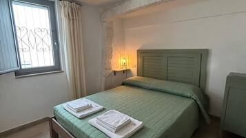 A bedroom with a bed, a nightstand, a lamp, and a window with curtains.