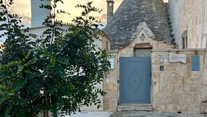 A stone building with a grey door and a small tree in front. - iCONICO - Authentic Trulli Experience (Cisternino)