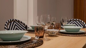 Une table à manger dressée avec des assiettes, des bols et des verres à vin, entourée de chaises aux motifs variés.