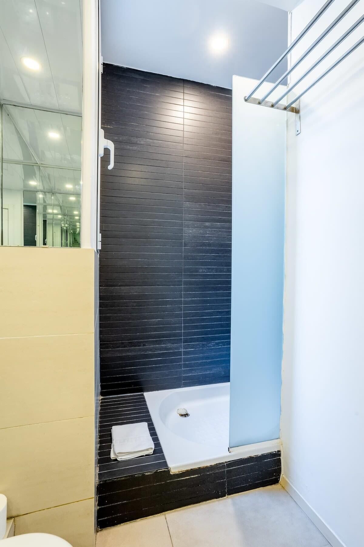 A modern bathroom with a glass shower enclosure, a black tiled wall, and a white bathtub.