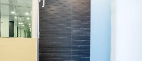 A modern bathroom with a glass shower enclosure, a black tiled wall, and a white bathtub.