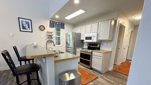 A compact kitchen with white cabinets, a stainless steel refrigerator, a microwave, and a stove. There is a small trash bin and a wooden dining table with two chairs. - Inviting Family Retreat w/Hot Tub in Driggs (Driggs)
