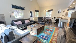 A spacious living area with a sofa, armchairs, a coffee table, and a dining table with chairs. There is a kitchen area with a sink and a trash can. - Inviting Family Retreat w/Hot Tub in Driggs (Driggs)