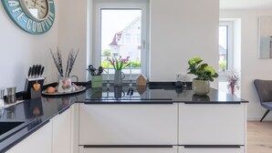 A modern kitchen with a black countertop, white cabinets, and a window with a view of buildings.